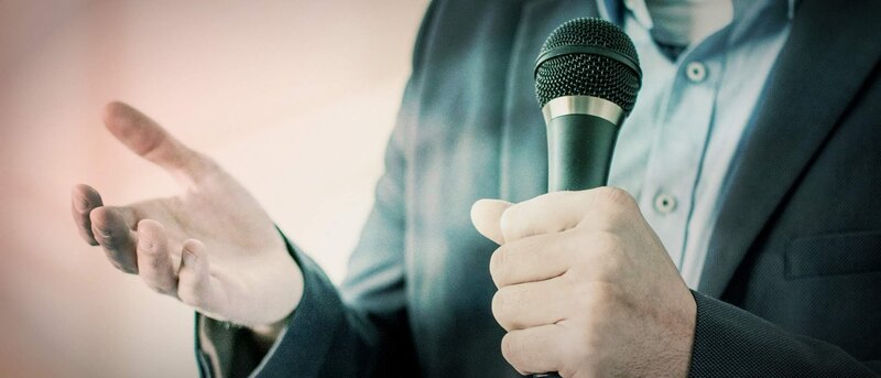 Person hält einen Vortrag mit einem Mikrofon in der Hand